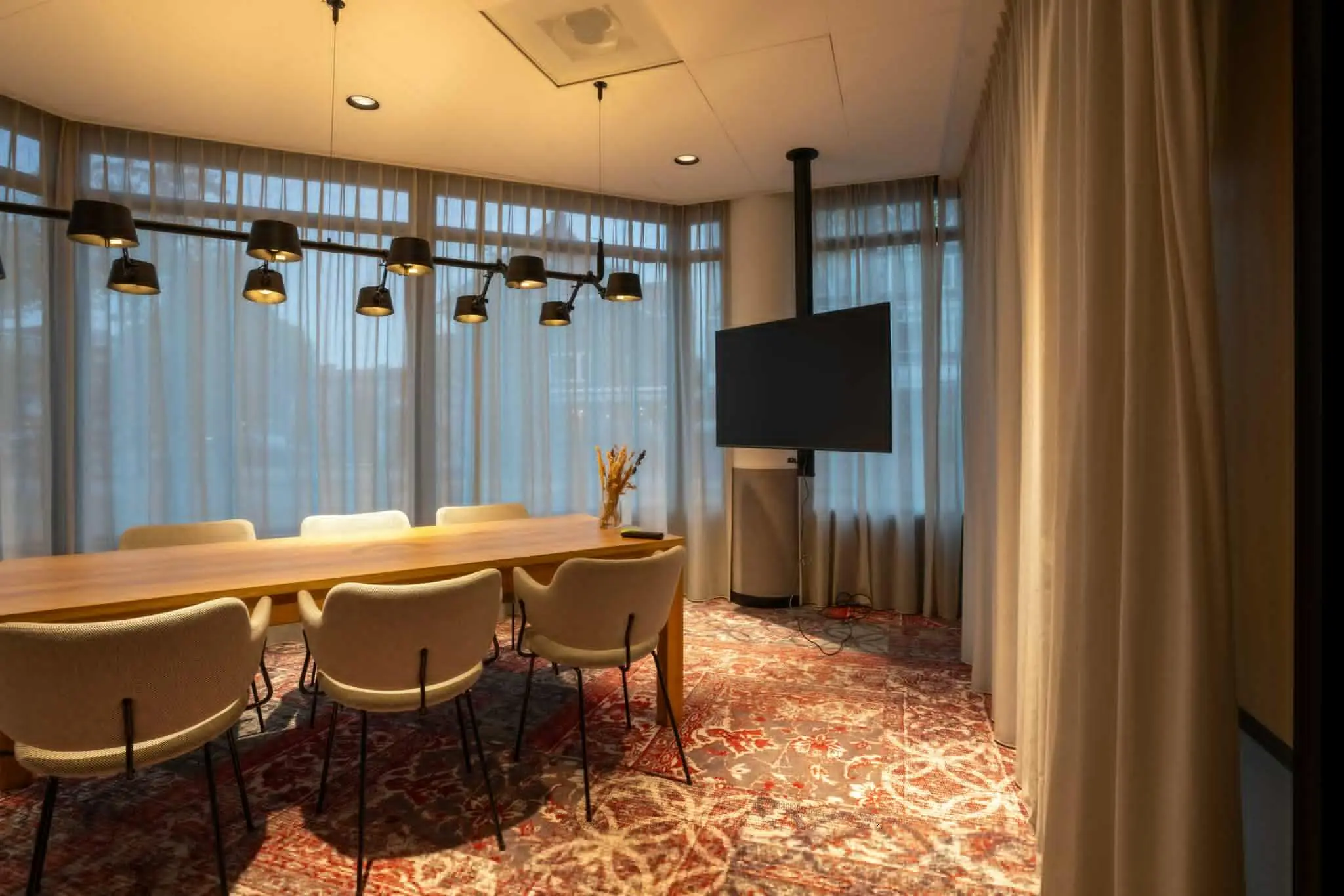 Vergaderruimte aan de 1e Hogeweg met lange houten tafel, beige stoelen, moderne verlichting en een groot presentatiescherm.